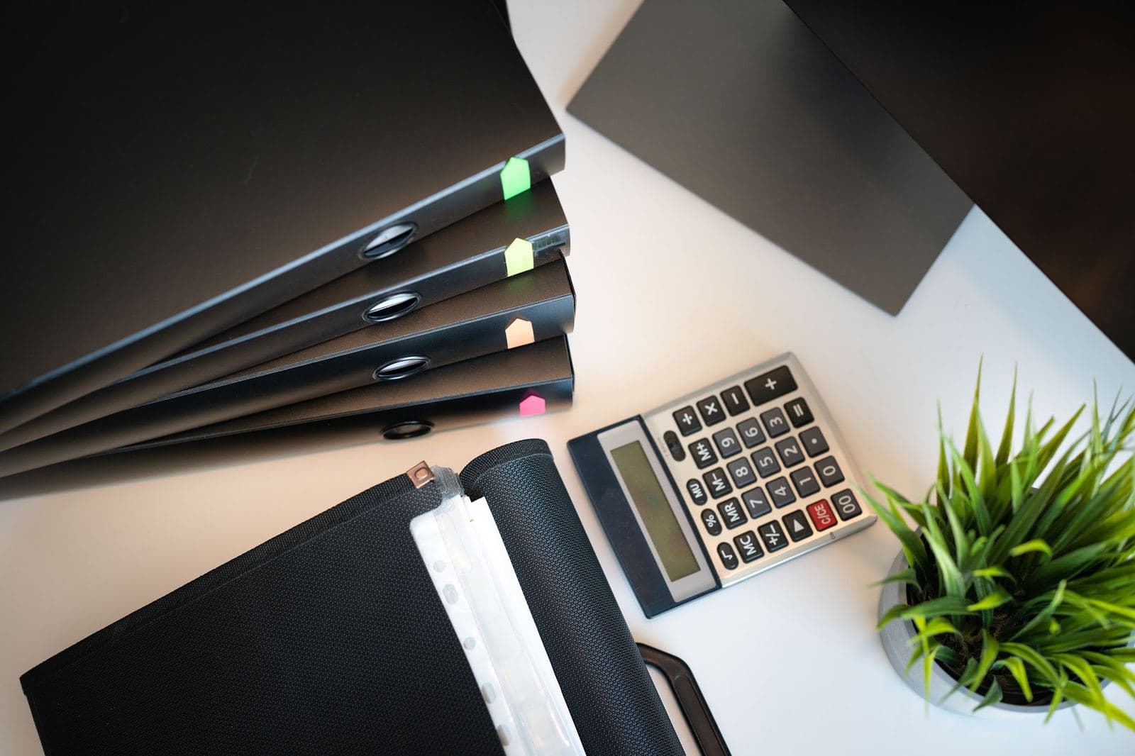 Ring binders with coloured index tabs, a calculator and a small plant on a desk.