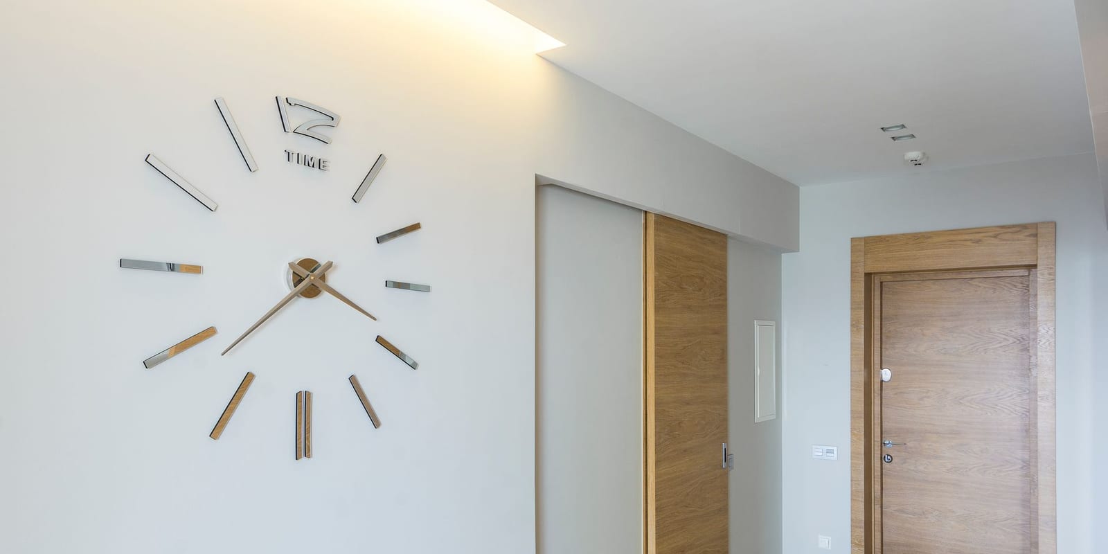 A minimalist wall clock in a room with pale wooden doors.