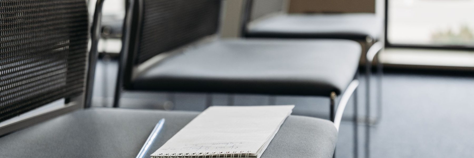 An open notebook and pen resting on a chair in a room set out for a meeting.