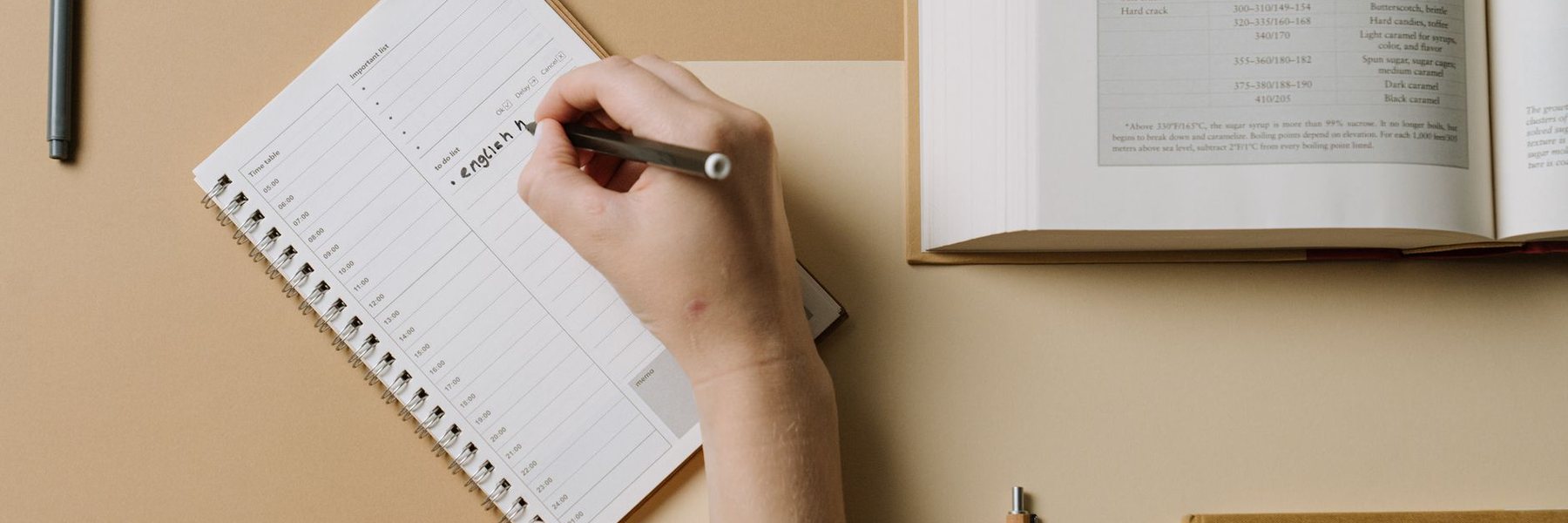 A hand writing in a lined notebook beside an open book.